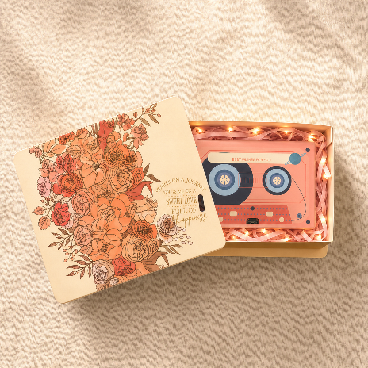Cassette audio rose dans un coffret cadeau illustré de fleurs, posé sur un tissu beige